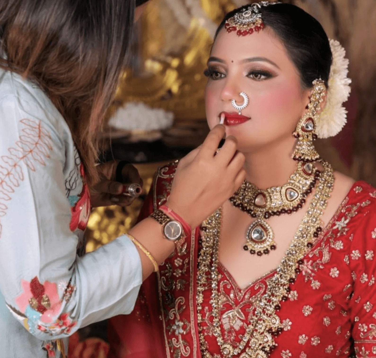Shalinee applying bridal makeup to an Indian bride in royal red wedding attire